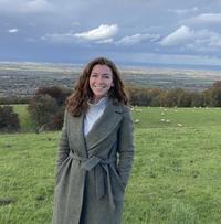 Molly standing in a field, wearing a grey coat