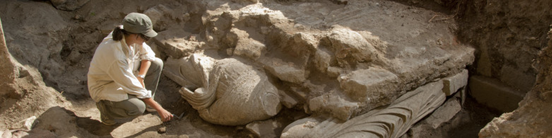 A woman digs in a trench. She wears a hat to protect her from the sun
