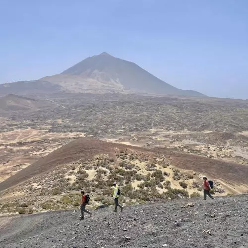 3 people walk along a dusty road, a mountain in the backround