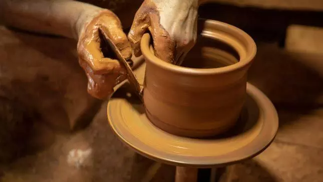 photo of a potter's hands making a vessel out of clay on a potter's wheel
