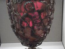 Lycurgus cup on display, lit from behind, showing the red color effect of the dichroic glass on transmitted light. Photo from Wikipedia by JohnBod