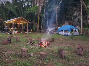 Photo of the main camp site with a fire burning, surrounding by cut tree stumps for chairs